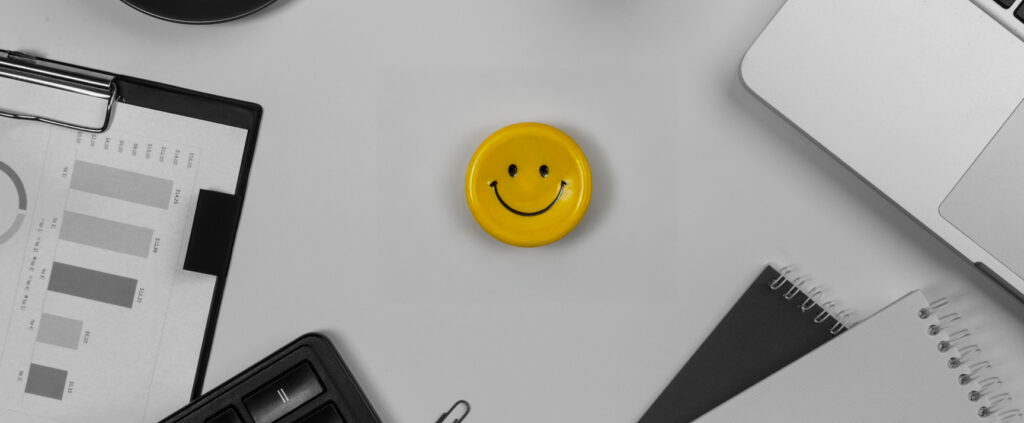 A Button With A Smile In The Center Of A Desk With A Coputer And Files