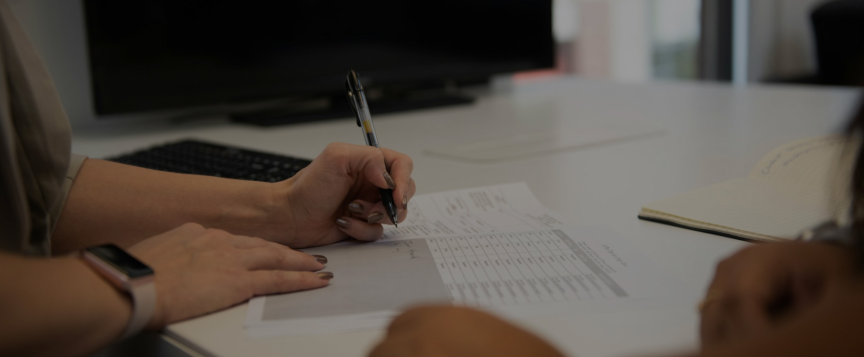 Close Up Of Woman Filling Out Paperwork At Doctors Office